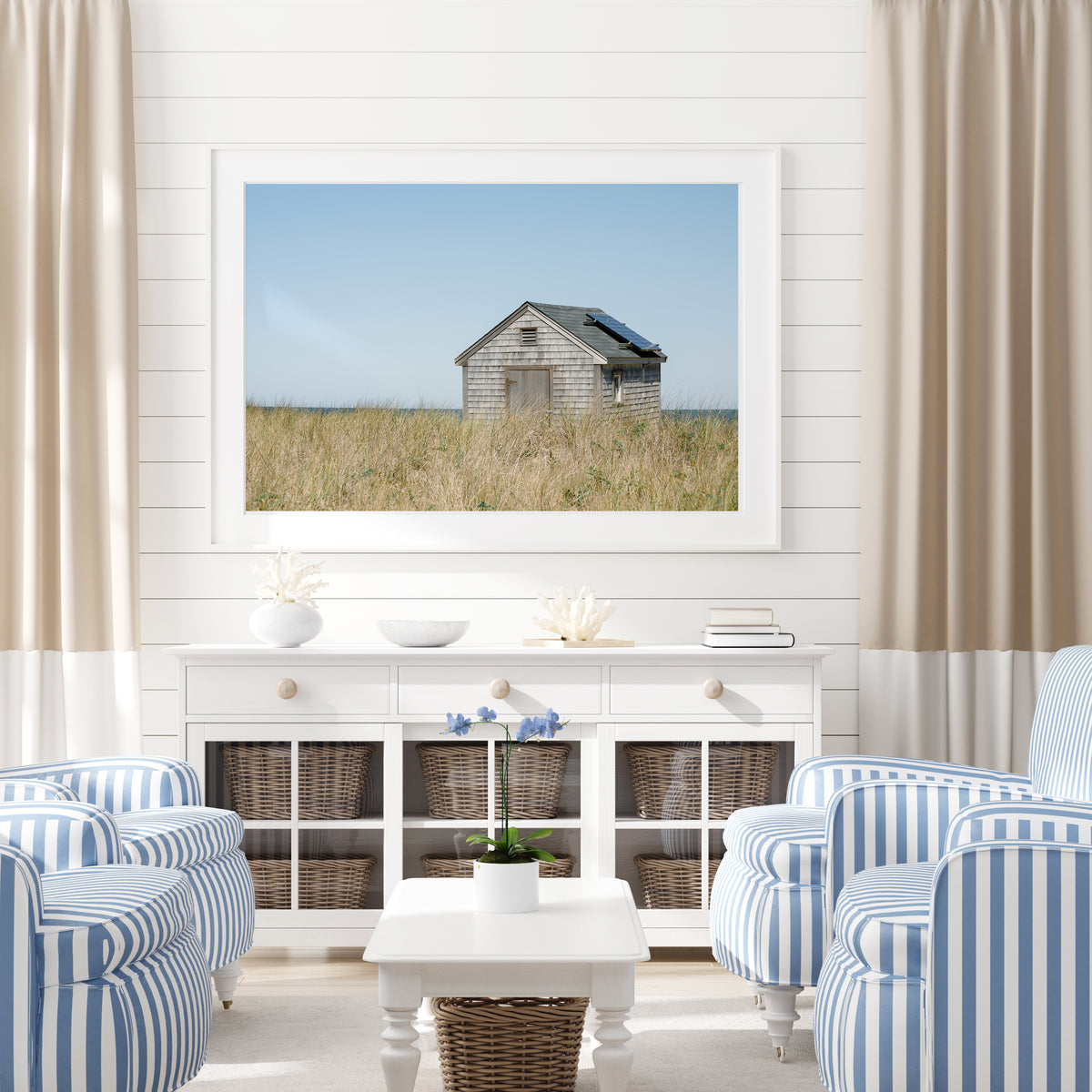 Color fine art photograph of a weathered grey shingle beach cottage alone in golden dune grass on Nantucket Island — ocean visible on the horizon under a wide pale blue sky