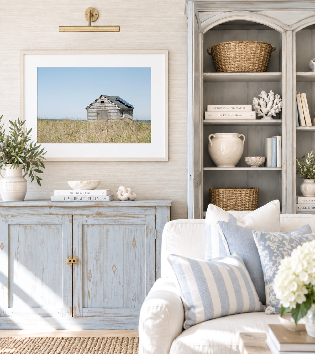 Color fine art photograph of a weathered grey shingle beach cottage alone in golden dune grass on Nantucket Island — ocean visible on the horizon under a wide pale blue sky