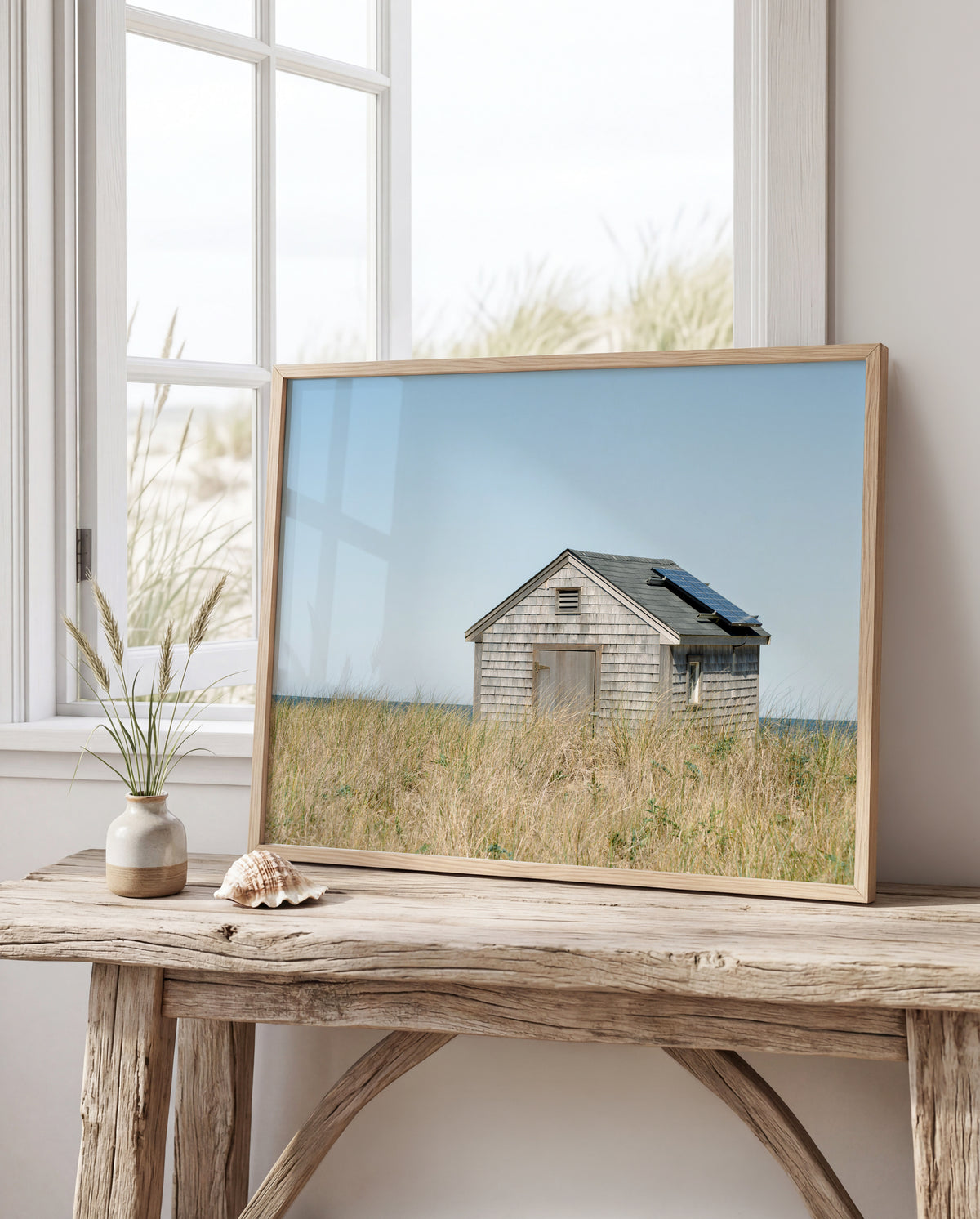Color fine art photograph of a weathered grey shingle beach cottage alone in golden dune grass on Nantucket Island — ocean visible on the horizon under a wide pale blue sky