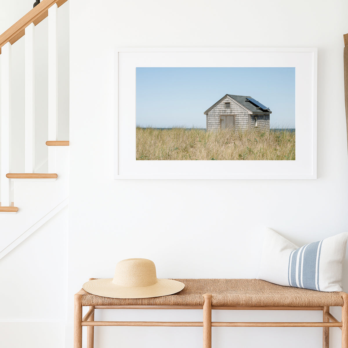 Color fine art photograph of a weathered grey shingle beach cottage alone in golden dune grass on Nantucket Island — ocean visible on the horizon under a wide pale blue sky