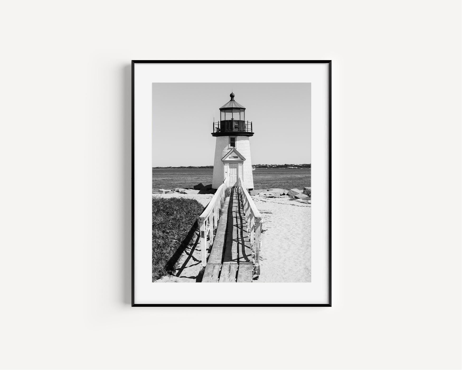 Black and white fine art photograph of Brant Point Lighthouse on Nantucket Island — wooden boardwalk leading to the white lighthouse tower with Nantucket Harbor in the background