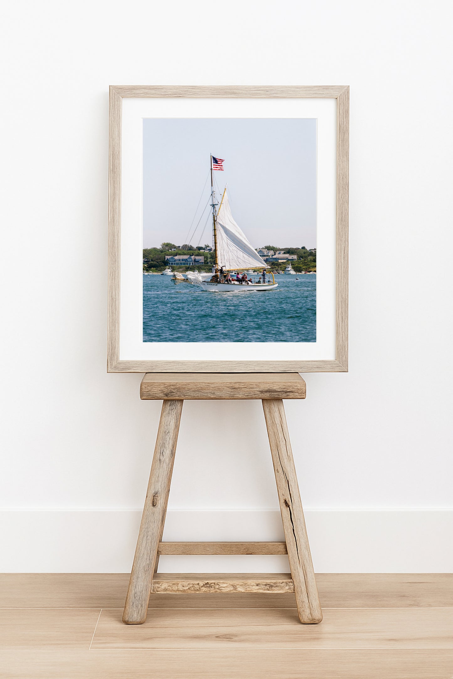 Sailboat cruising in Nantucket Harbor with white sails raised and an American flag flying, photographed on a clear summer day along the New England coastline.