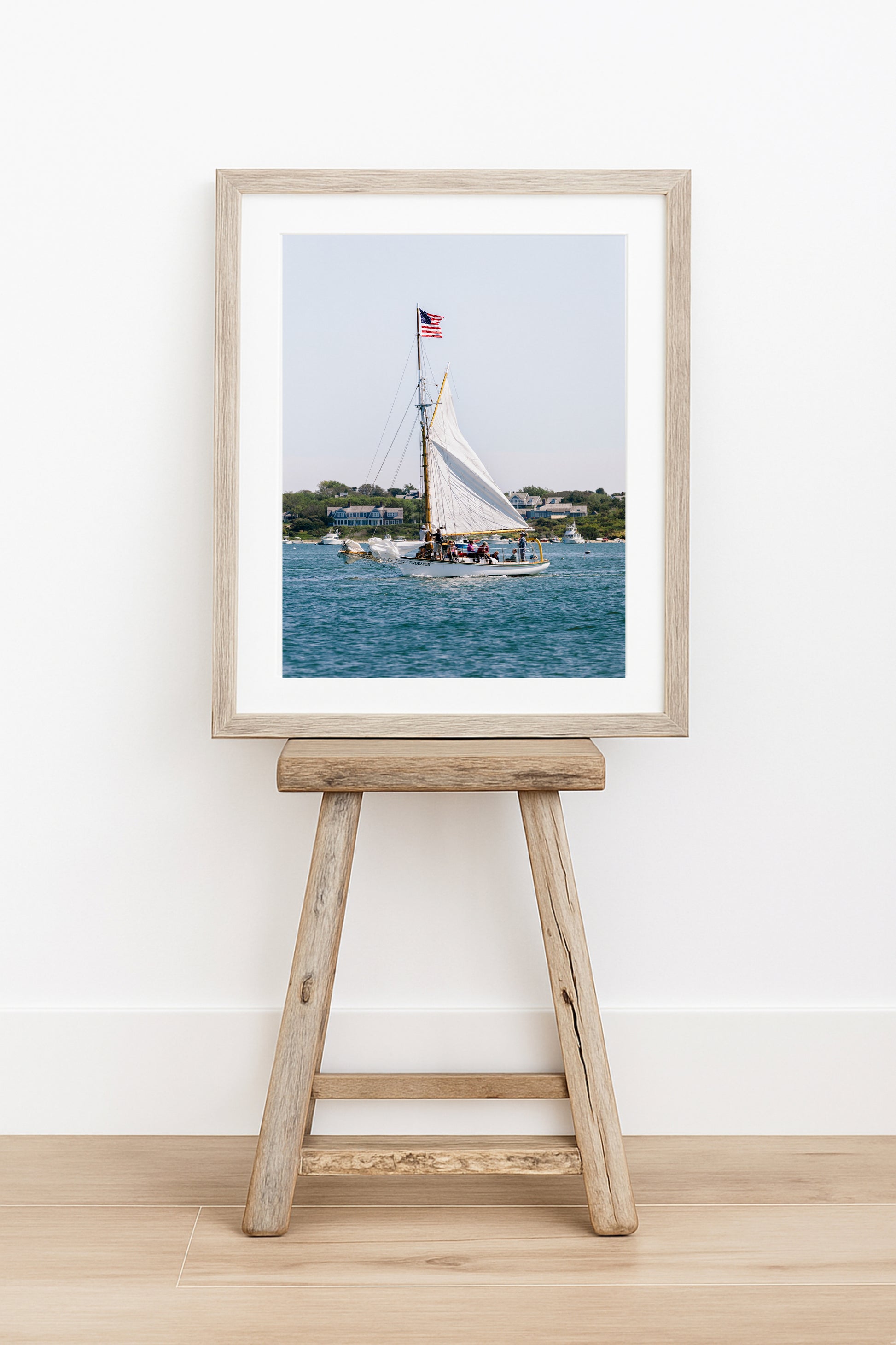 Sailboat cruising in Nantucket Harbor with white sails raised and an American flag flying, photographed on a clear summer day along the New England coastline.