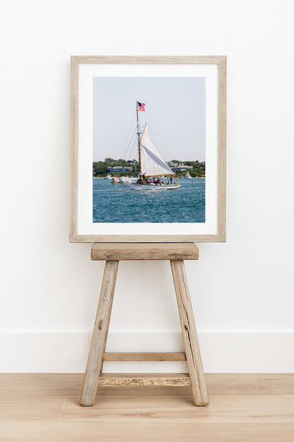 Sailboat cruising in Nantucket Harbor with white sails raised and an American flag flying, photographed on a clear summer day along the New England coastline.