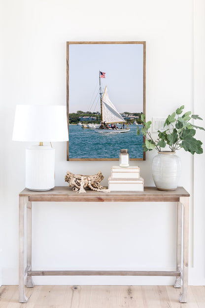 Sailboat cruising in Nantucket Harbor with white sails raised and an American flag flying, photographed on a clear summer day along the New England coastline.