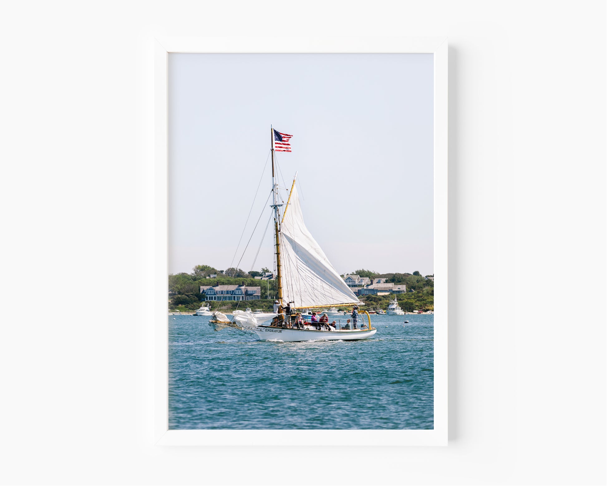Sailboat cruising in Nantucket Harbor with white sails raised and an American flag flying, photographed on a clear summer day along the New England coastline.