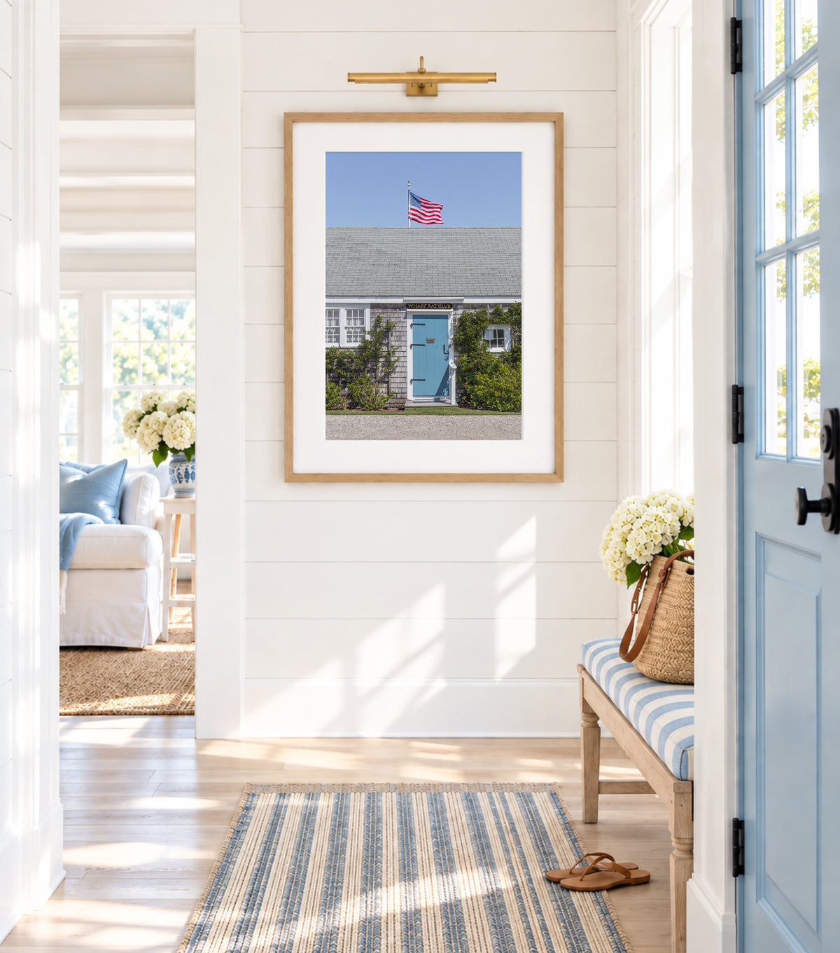 Color fine art photograph of the Wharf Rat Club on Nantucket — weathered grey shingle cottage with a powder blue door, climbing vines, and an American flag flying above the roofline against a blue summer sky