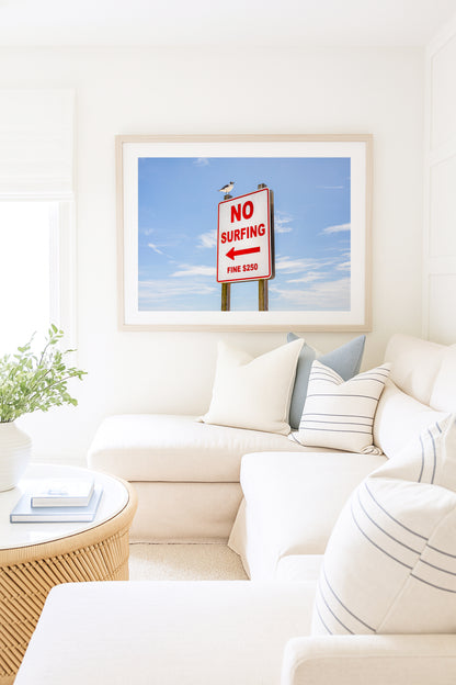 Color fine art photograph of a red and white No Surfing Fine $250 sign at Wrightsville Beach in Wilmington, North Carolina — a seagull perched on top of the sign against a blue sky