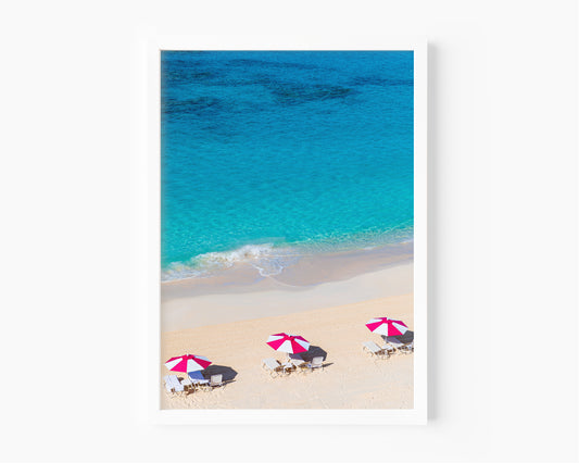 Vertical aerial view of three pink beach umbrellas on a Bermuda shoreline with turquoise ocean