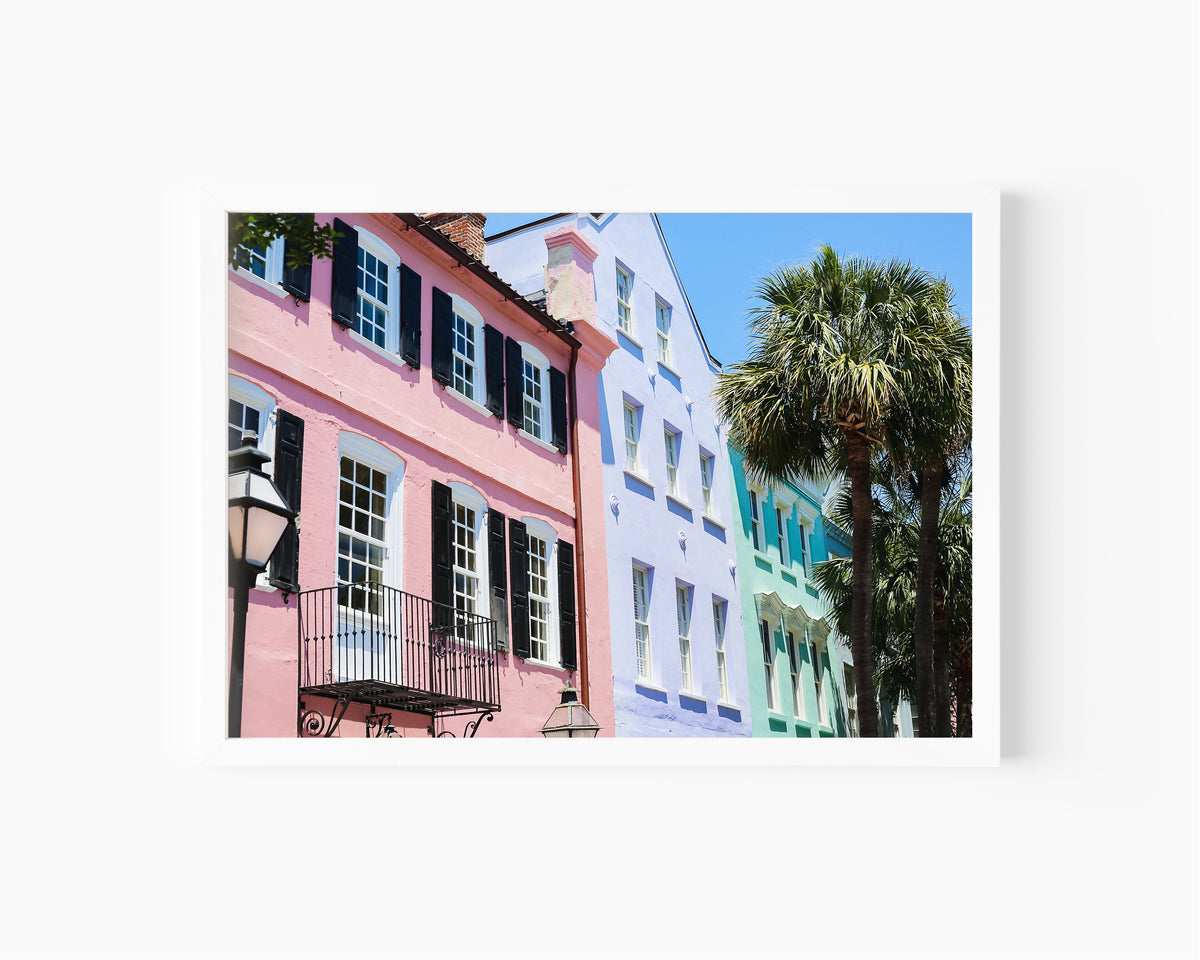Color fine art photograph of Rainbow Row on East Bay Street in Charleston, South Carolina — pink, lavender, and mint green pastel facades with wrought iron balconies and palm trees against a blue sky