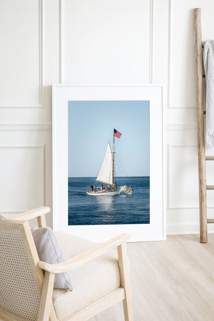 Nantucket Harbor sailboat photography print, classic wooden sailing vessel with American flag on deep blue water, coastal nautical wall art for beach house, living room, or home office