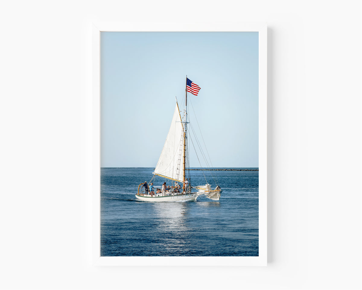 Nantucket Harbor sailboat photography print, classic wooden sailing vessel with American flag on deep blue water, coastal nautical wall art for beach house, living room, or home office