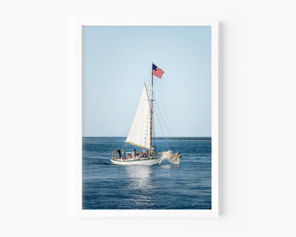 Nantucket Harbor sailboat photography print, classic wooden sailing vessel with American flag on deep blue water, coastal nautical wall art for beach house, living room, or home office