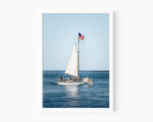 Nantucket Harbor sailboat photography print, classic wooden sailing vessel with American flag on deep blue water, coastal nautical wall art for beach house, living room, or home office