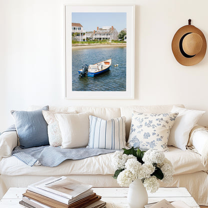 Vertical beach photography print of a small blue boat floating in Nantucket harbor, with Cape Cod-style houses and sandy shoreline in the background — perfect for nautical home decor and coastal wall art.